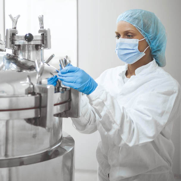 A young female skilled worker in protective gear operates a high-tech equipment in a pharmaceutical production facility, ensuring the precise mixing of substances to produce life-saving medications. Highlighting the dedication and precision required in the industry.