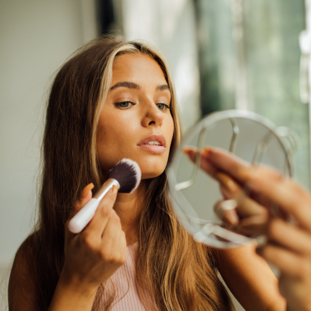 Young woman applying makeup in the mirror